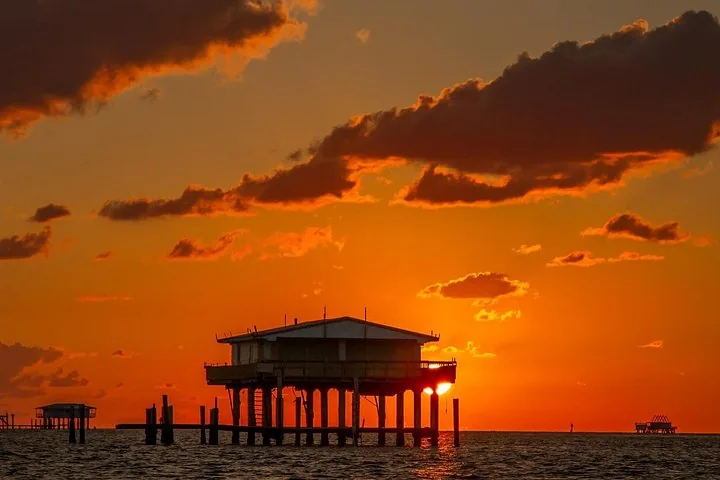 Silhouetten van Stiltsville-huizen boven het water tegen een levendige oranje zonsondergang