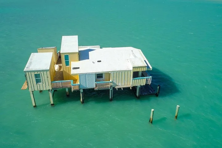 Luchtfoto van een geel houten paalhuis omringd door turquoise water